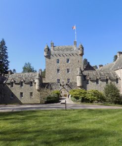 Cawdor Castle fills this image, below a cloudless blue sky on the tour that also visits Culloden and Clava. The castle is grey stone, with green lawns in front, some shrubs either side of the small drawbridge, and large trees behind. The 1300s Keep is square and four storeys high with battlements and a pepper-pot tower at each corner. It is only two windows wide on each side. There are four other wings, in front and to each side, all built of matching stone, but dating from the 1600's, 1700's and 1800's. Although organic, the resulting building is pleasingly consistent and attractive.