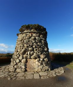 A large monument with bushes on the top stands under a vivid blue sky on an open moor on our Outlander Tour from Invergordon.
