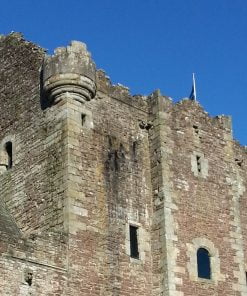 The top of the ruined Doune Castle Keep, visited on our Highlands Tour, is seen here against a vivid blue sky. There is a flagpole situated on top of the keep, from which a Scottish flag hangs.