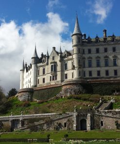 A huge chateau-style castle dominates this image, standing above us on a rise. Many-turreted and white, it stands under a blue, but cloudy, sky and gardens are at the castle's feet.