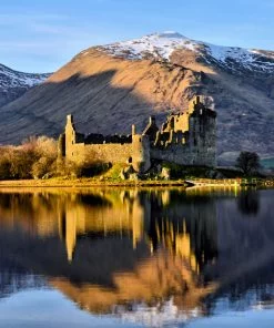 There is a blue sky with two snow capped mountains. The foreground is a lake, and the centrepiece is a ruined castle projecting into the lake on a wooded spit of land. This whole picture is then imperfectly reflected in the rippled surface of the lake.