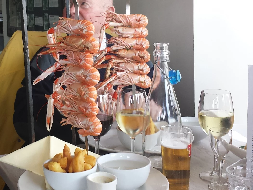 Tall standing skewers on a restaurant table, on our Ardvreck Castle and Geopark Tour. Each skewer holds up to 7 langoustine. Wines, a lager and a bowl of chips also adorn the table.