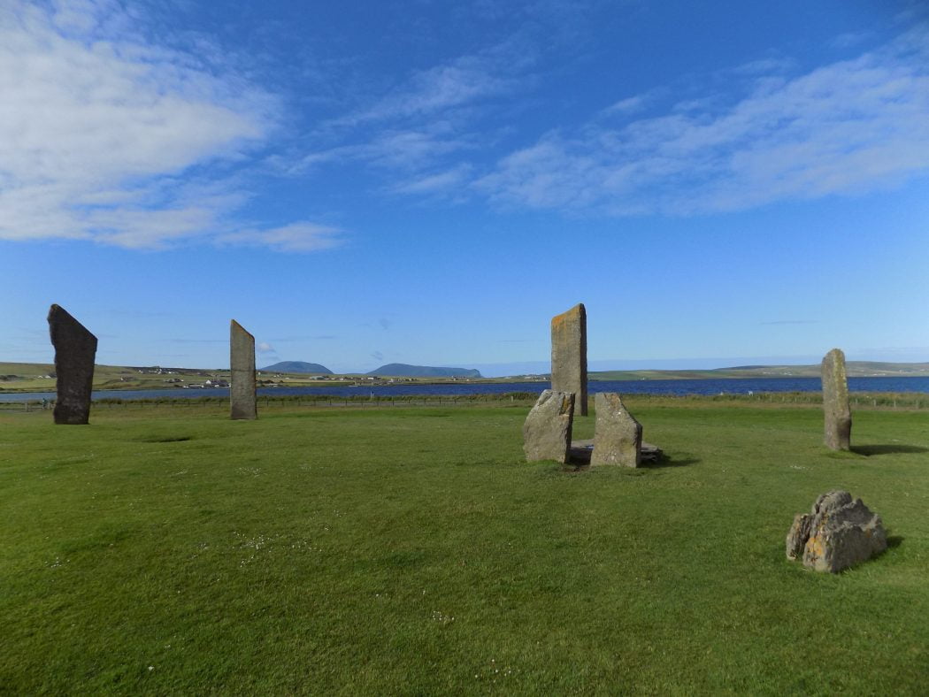 wide image of seven of the Standing Stones of Stenness on our Orkney - Two Day Tour. Behind is the Loch of Stenness, lots of distant farms and farmland and in the far background the high hills of the island of Hoy.