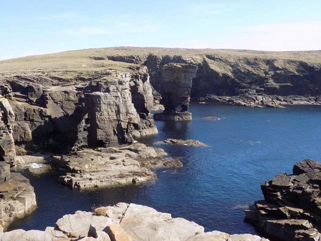 wide image of the sunny cliff scenery and rock formations known as Yesnaby Castle sea stack on Orkney. Avery light blue sky, and deep blue sea.