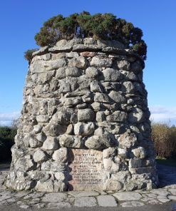 A large monument with bushes on the top stands 20 feet tall under a vivid blue sky on an open moor on our Loch Ness with Culloden and Urquhart Castle Tour