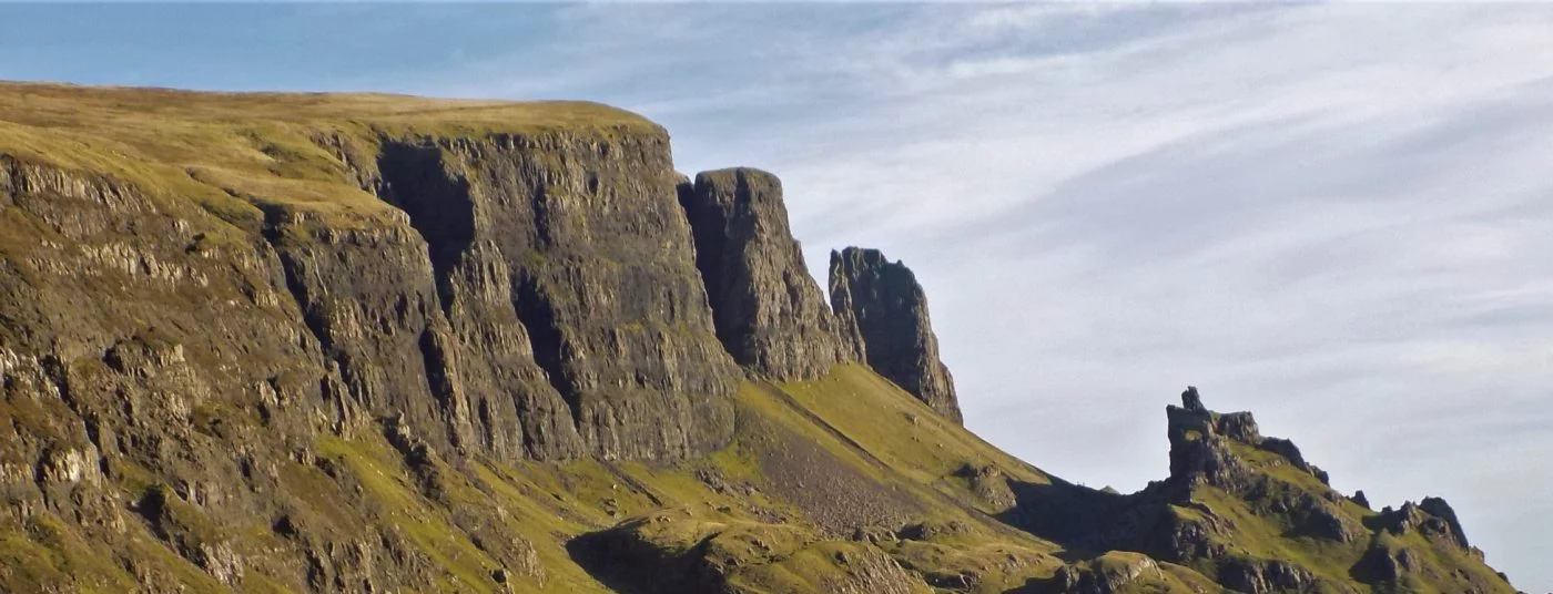 This wide picture is of a major landslip on the Trotternish Ridge. The sky above is blue and the grass is green, but overwhelmingly the great cliffs are black and shattered into cracks, chasms and pinnacles.The Quiraing on the Trotternish Peninsula on the Isle of Skye