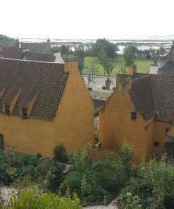 We are above a beautiful garden, which itself is behind a 1500's merchant palace, painted yellow and with pantiles on the roof. In front of the two buildings of the palace are some other old buildings, and to the left, a tolbooth tower. Beyond that, in the background, is the sea-shore.