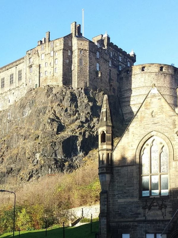 There is a church in the foreground. In the background a castle stands atop a great black rock, and above it all the sky is blue.
